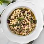 Round white bowl of Marinated White Beans, sitting on a green cloth.