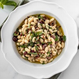 Round white bowl of Marinated White Beans, sitting on a green cloth.