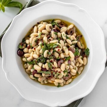 Round white bowl of Marinated White Beans, sitting on a green cloth.
