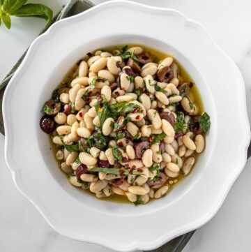Round white bowl of Marinated White Beans, sitting on a green cloth.