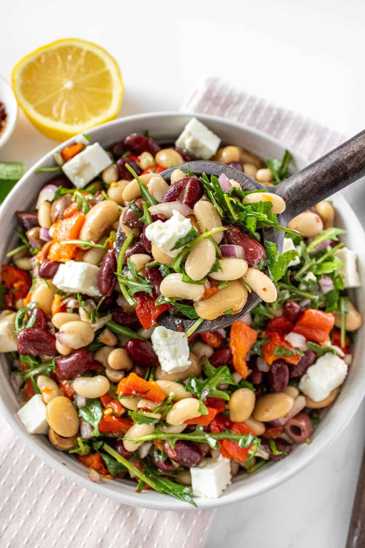 Spoon lifting up a serve of Mediterranean Bean Salad from a round white bowl.