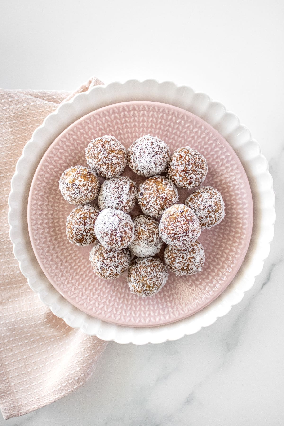 Pink plate sitting on a white plate, topped with Peanut Butter Bliss Balls.