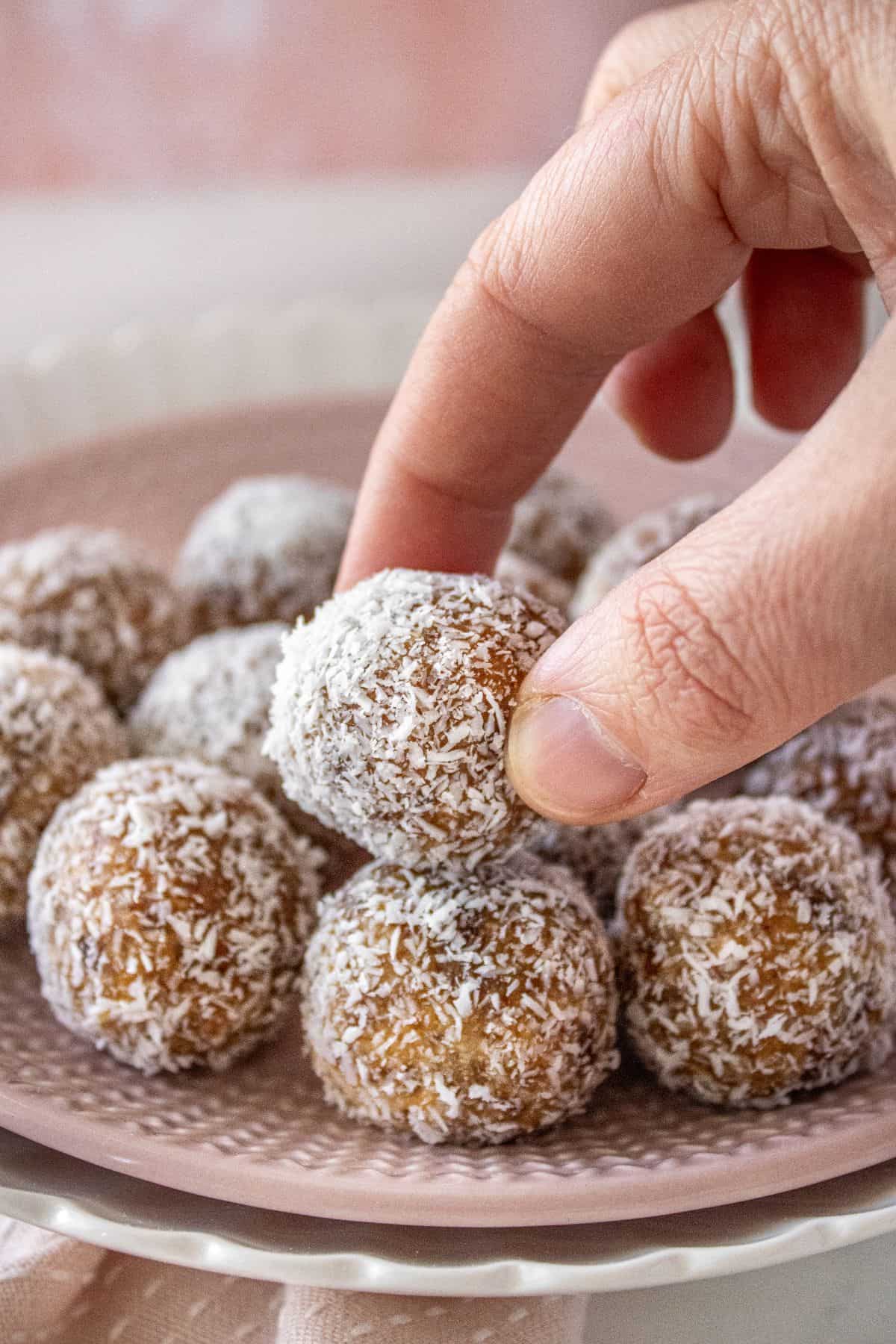 Hand reaching to pick up a Peanut Butter Bliss Ball from a pink plate.