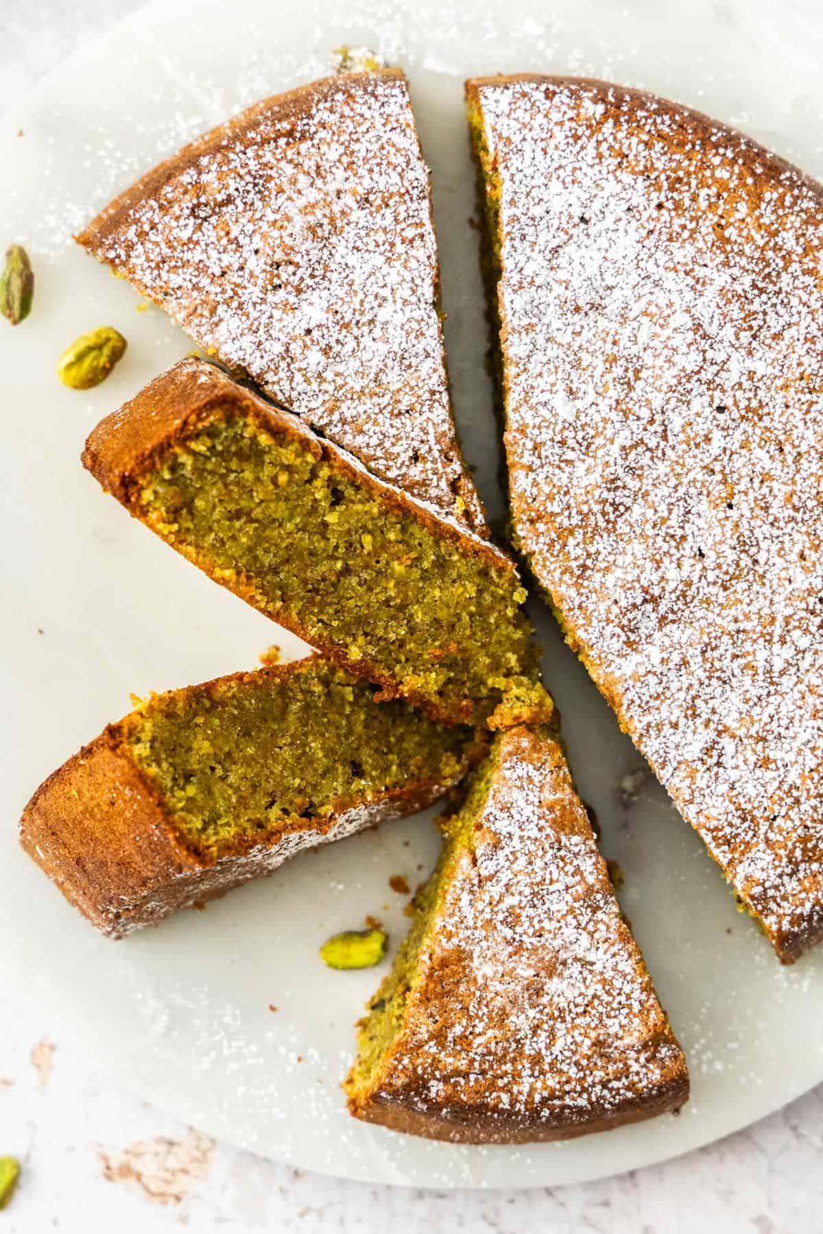 Pistachio Cake dusted with icing/powdered sugar, with some pieces cut.