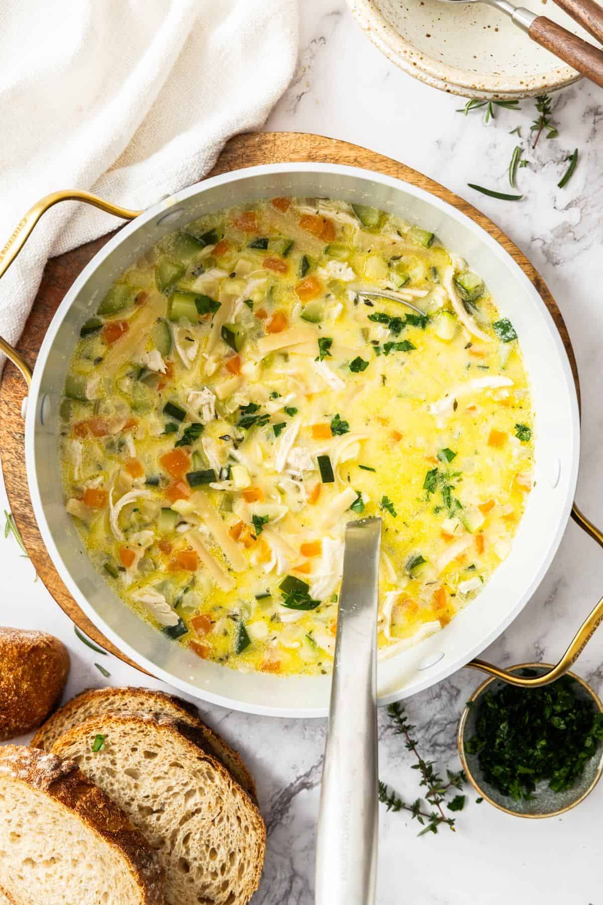 Large saucepan of Creamy Chicken Noodle Soup, with a ladle resting in pot.