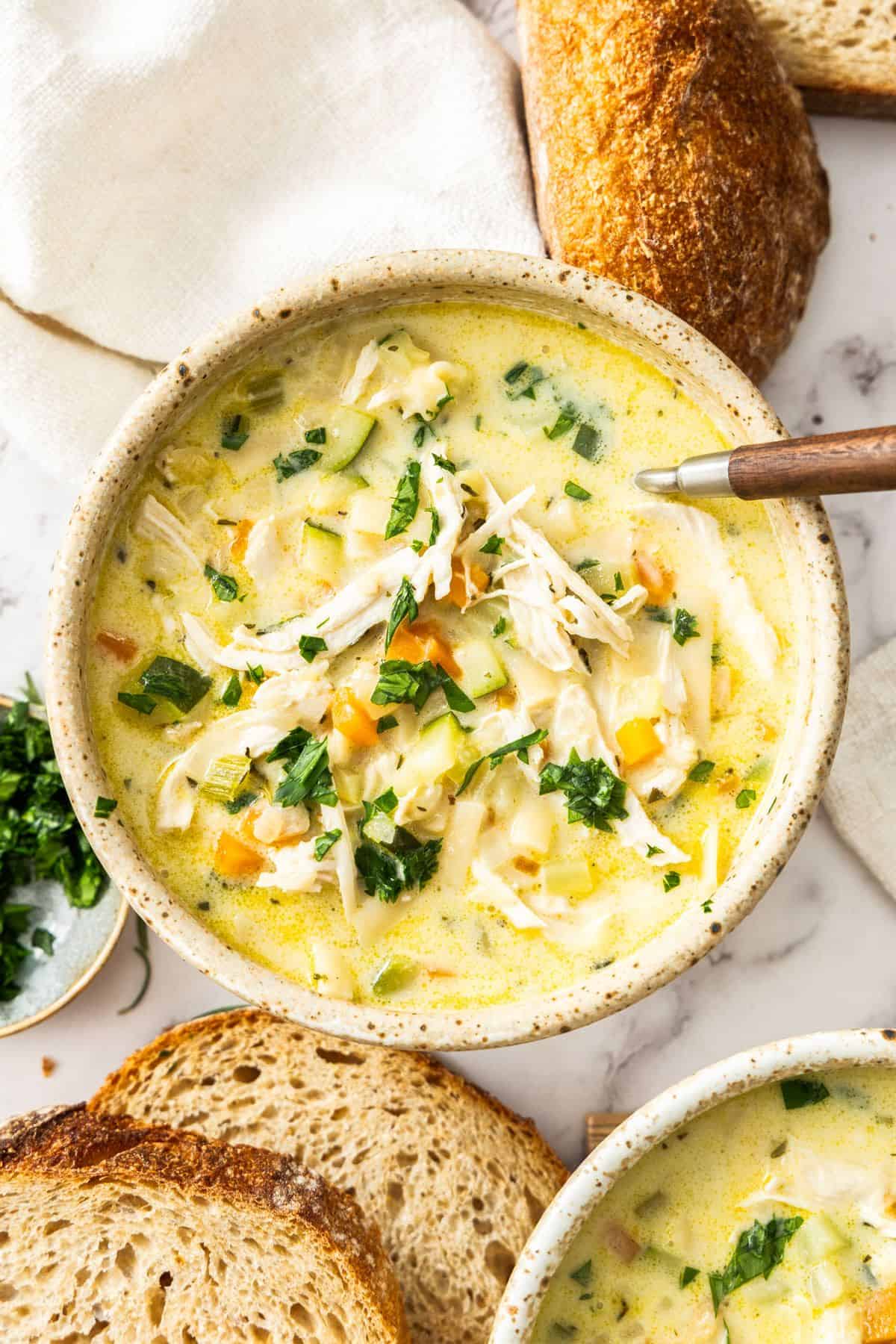 Bowls of Creamy Chicken Noodle Soup, garnished with some fresh parsley, with a spoon resting in bowl.