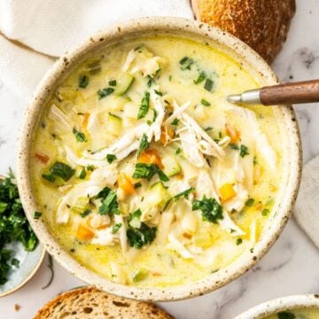Bowl of Creamy Chicken Noodle Soup, garnished with some fresh parsley, with a spoon resting in bowl.