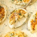 Large frying pan with Creamy Herb Chicken, with a spoon lifting up a piece of chicken.
