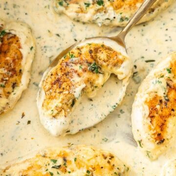 Large frying pan with Creamy Herb Chicken, with a spoon lifting up a piece of chicken.