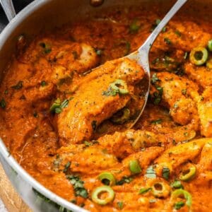 Creamy Red Pepper Chicken in a large frying pan, with a spoon lifting up a piece of chicken.