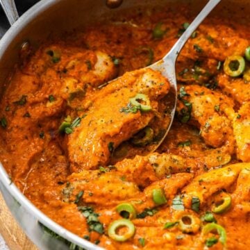 Creamy Red Pepper Chicken in a large frying pan, with a spoon lifting up a piece of chicken.