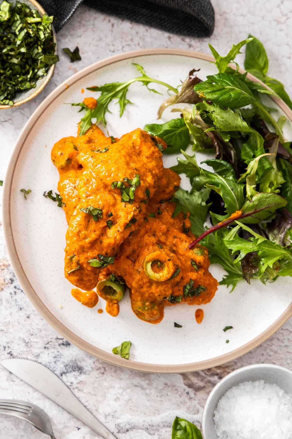 Serve of Creamy Red Pepper Chicken on a round white plate with a green side salad.