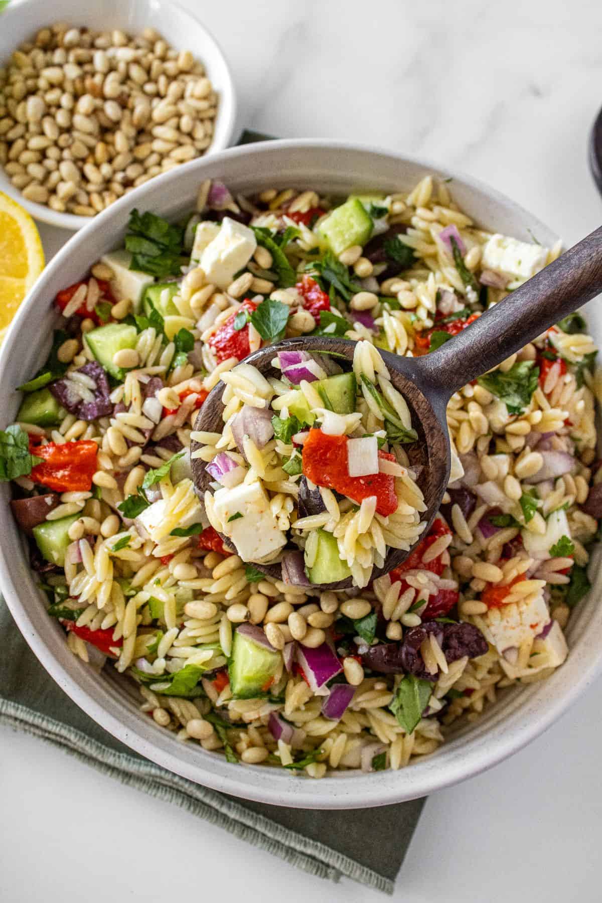 Round white bowl of Mediterranean Orzo Salad, on a green towel, with a some lifting up a scoop of salad.