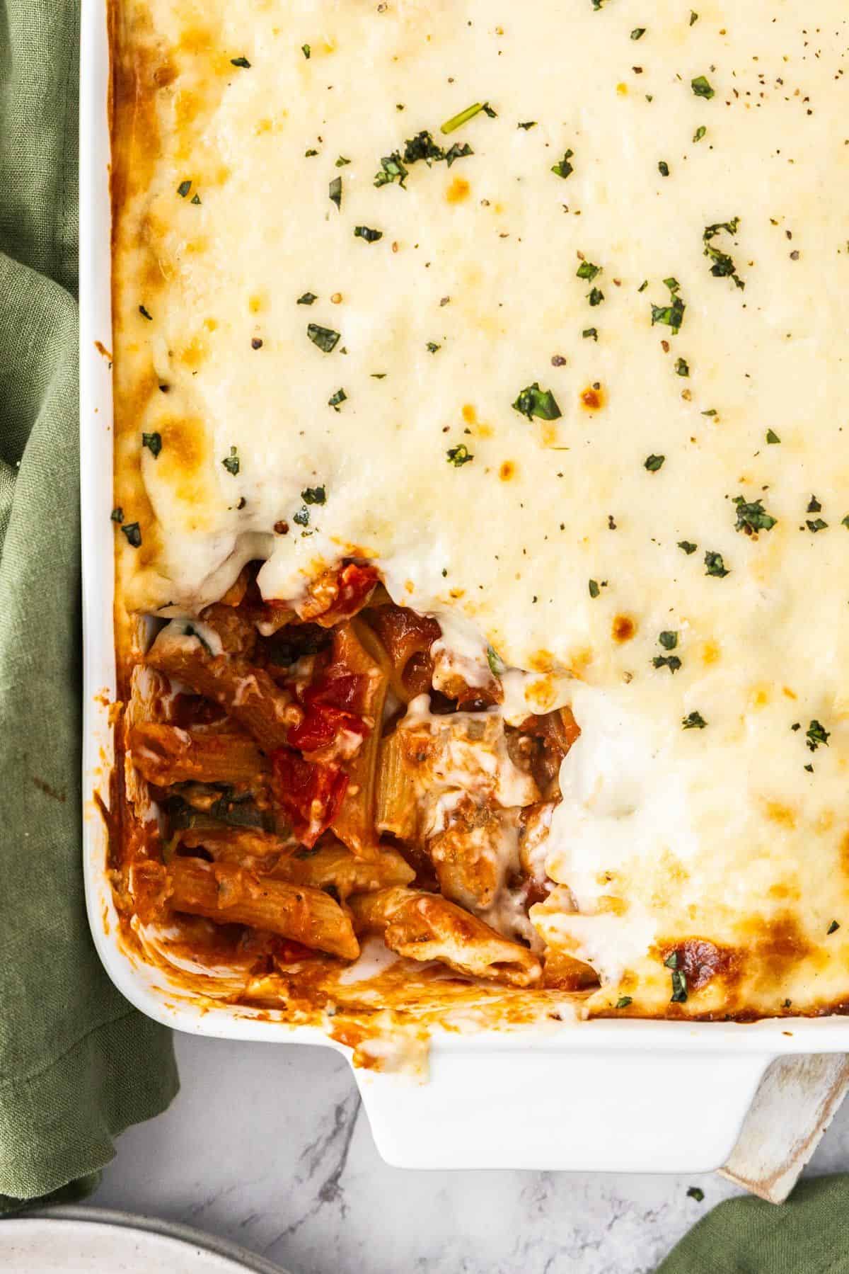 White rectangular dish of Mediterranean Sausage Pasta Bake, topped with a sprinkling of fresh parsley, with a scoop removed.
