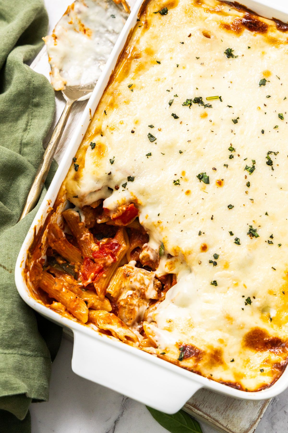 White rectangular dish of Mediterranean Sausage Pasta Bake, topped with a sprinkling of fresh parsley, with a scoop removed.