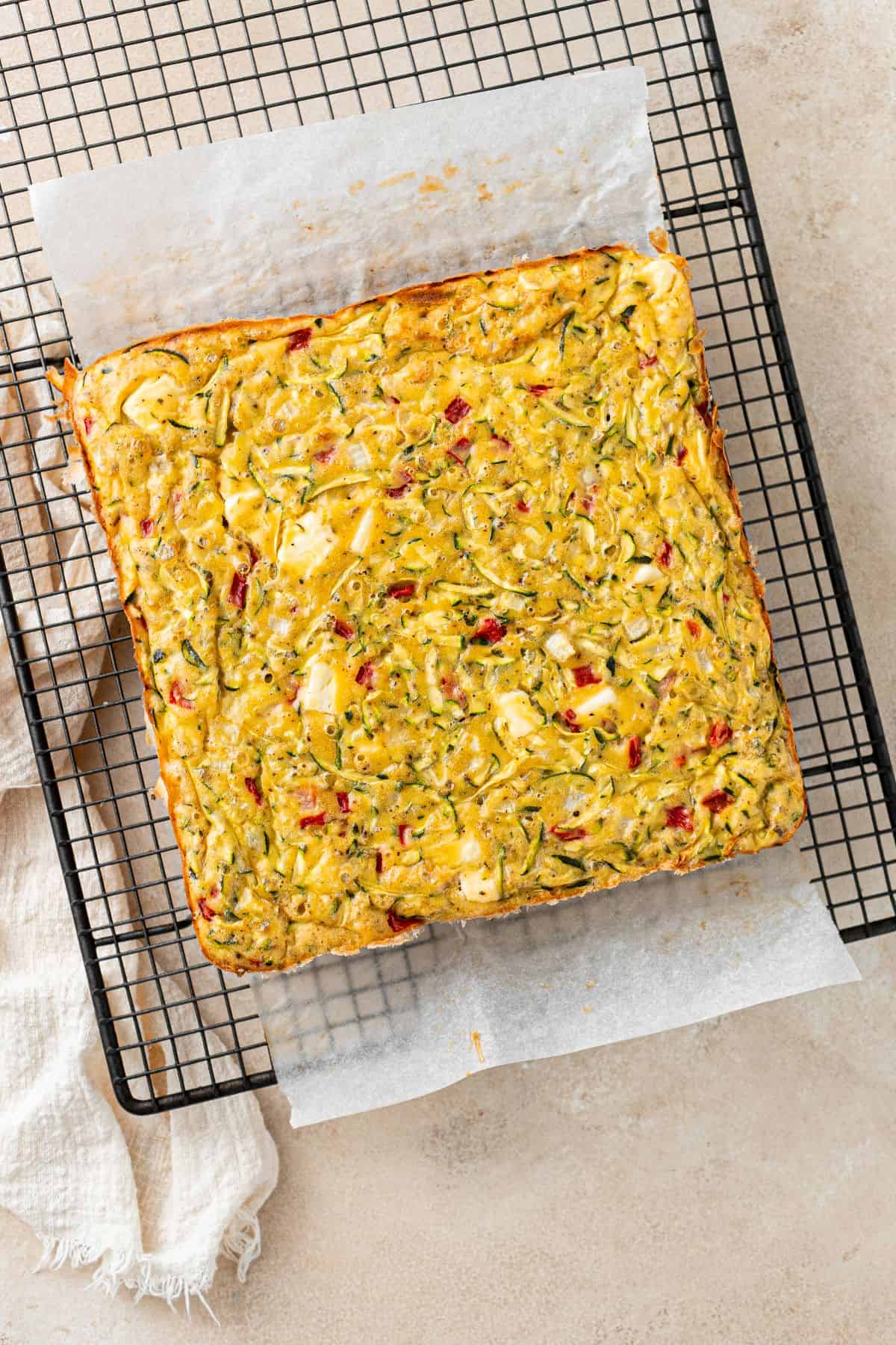 Whole baked Mediterranean Zucchini Slice on some baking paper and a cooling rack.
