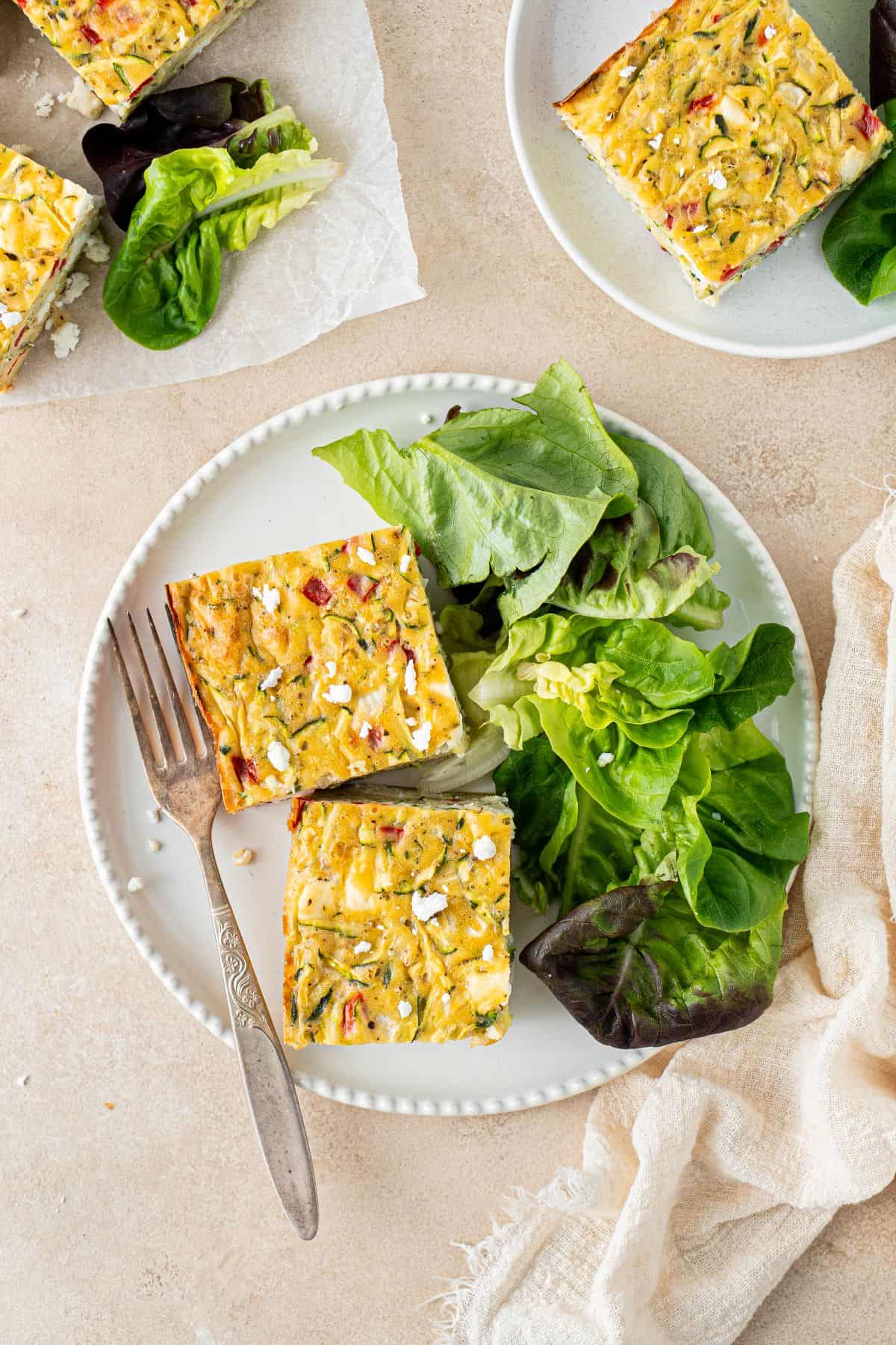 Plate with two squares of Zucchini Slice, a green salad and a fork.