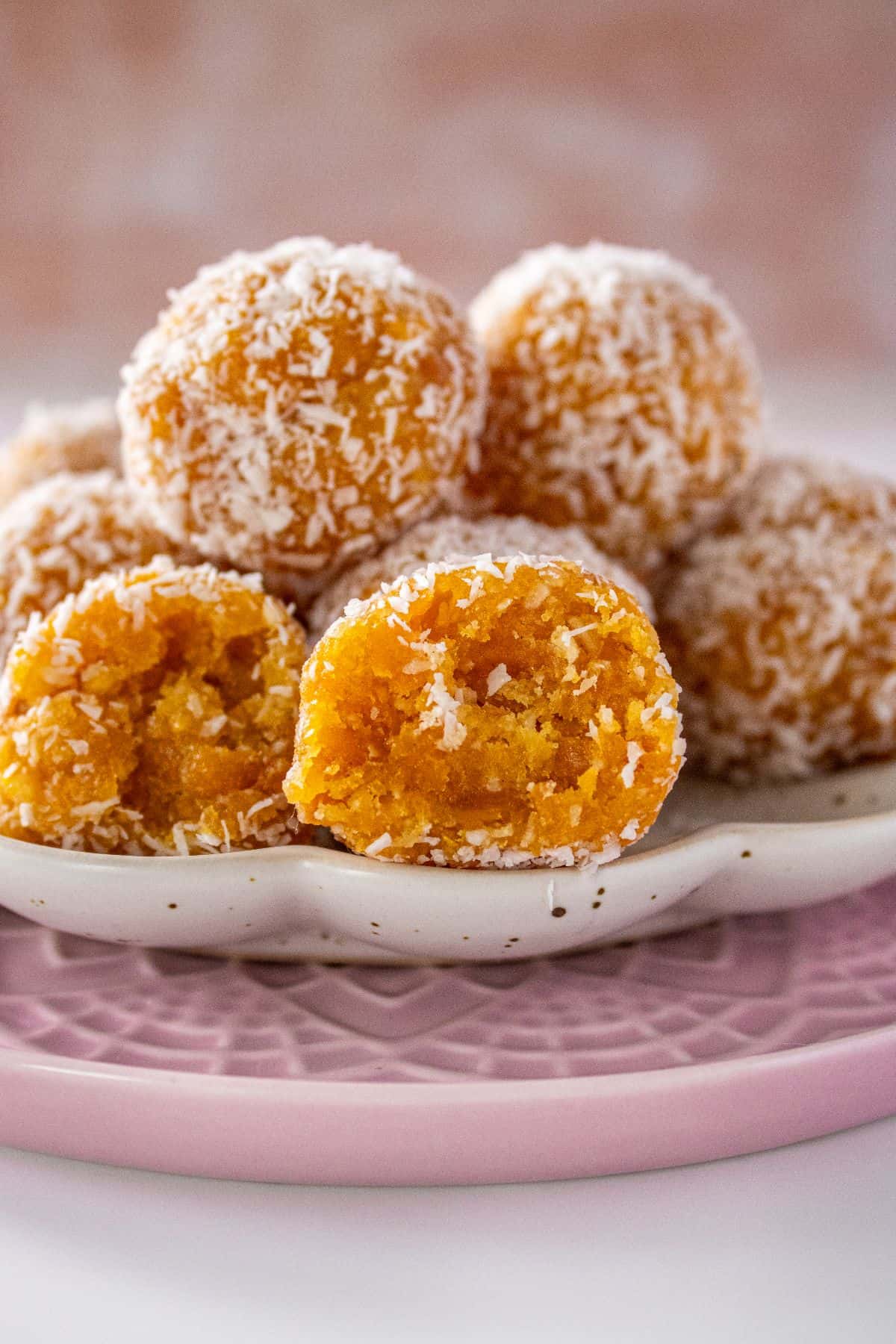 Two plates, one pink and one white, with a pile of Peach Bliss Balls on top, one cut in half to show the inside.
