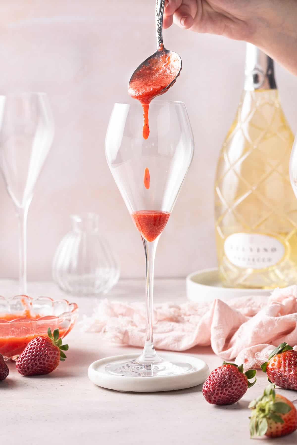 Spoon adding some strawberry puree to a champagne glass.