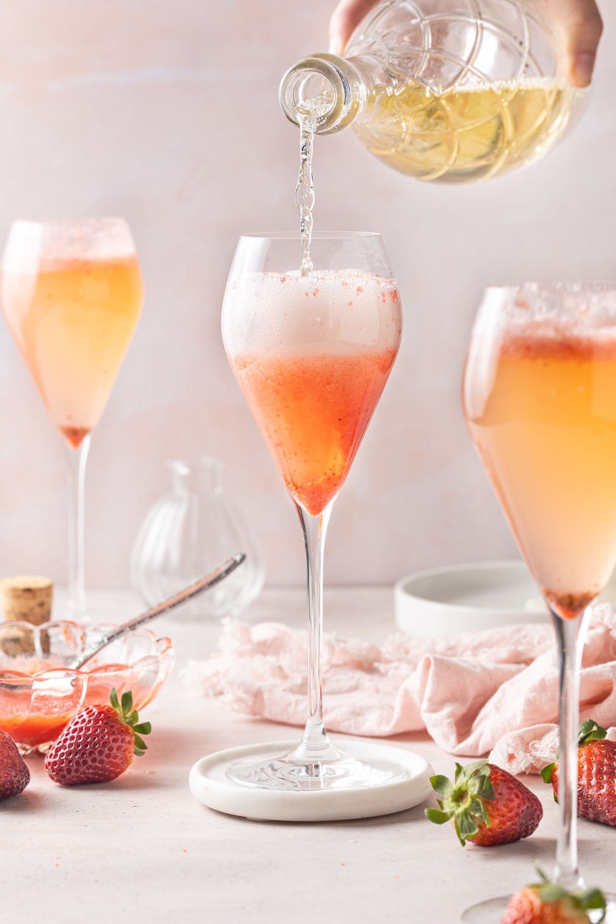 A bottle of Prosecco pouring into a champagne glass that contains some strawberry puree.