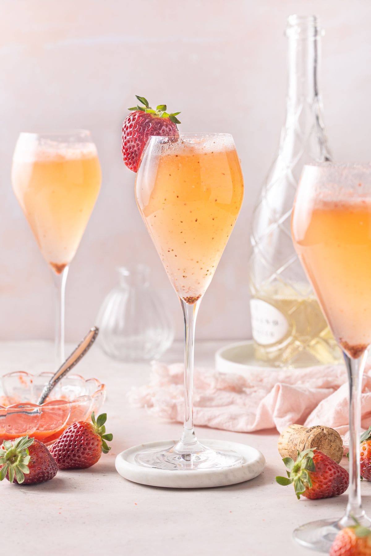 Three champagne glasses containing Strawberry Prosecco, one garnished with a strawberry.