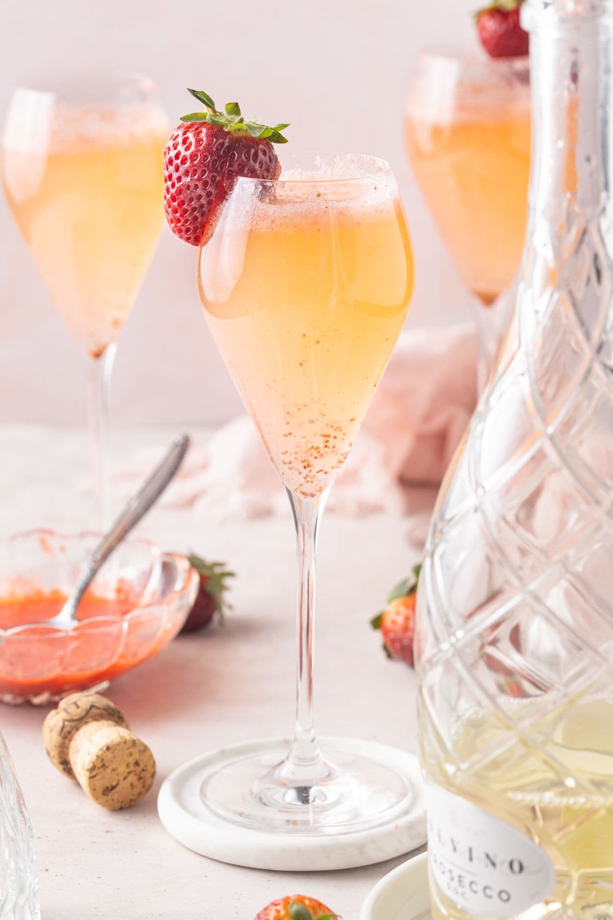 Three champagne glasses containing Strawberry Prosecco, one garnished with a strawberry.