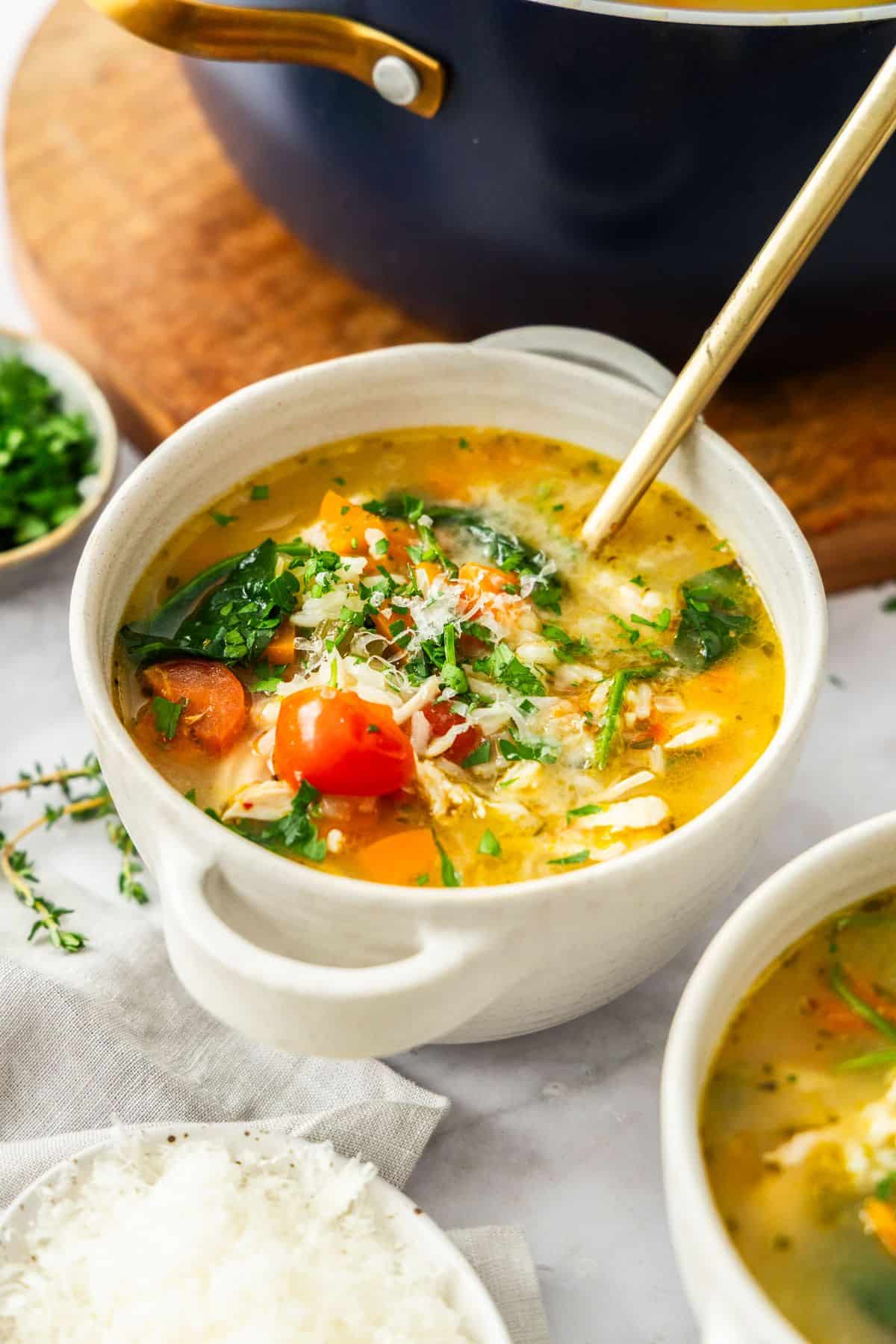 Small white bowl of Mediterranean Chicken and Rice Soup with a gold spoon resting in the bowl.