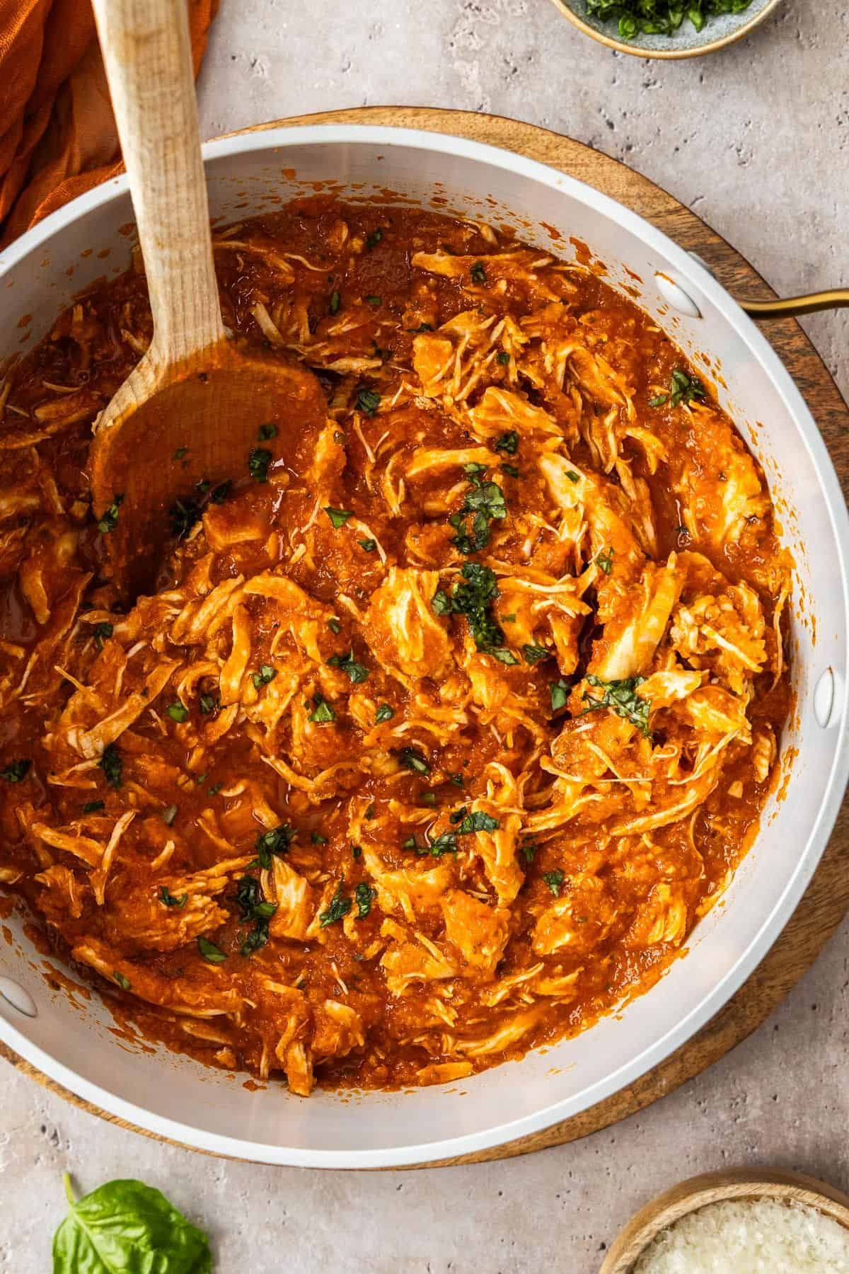 Large saucepan of Mediterranean Pulled Chicken, with a wooden spoon resting in pot.