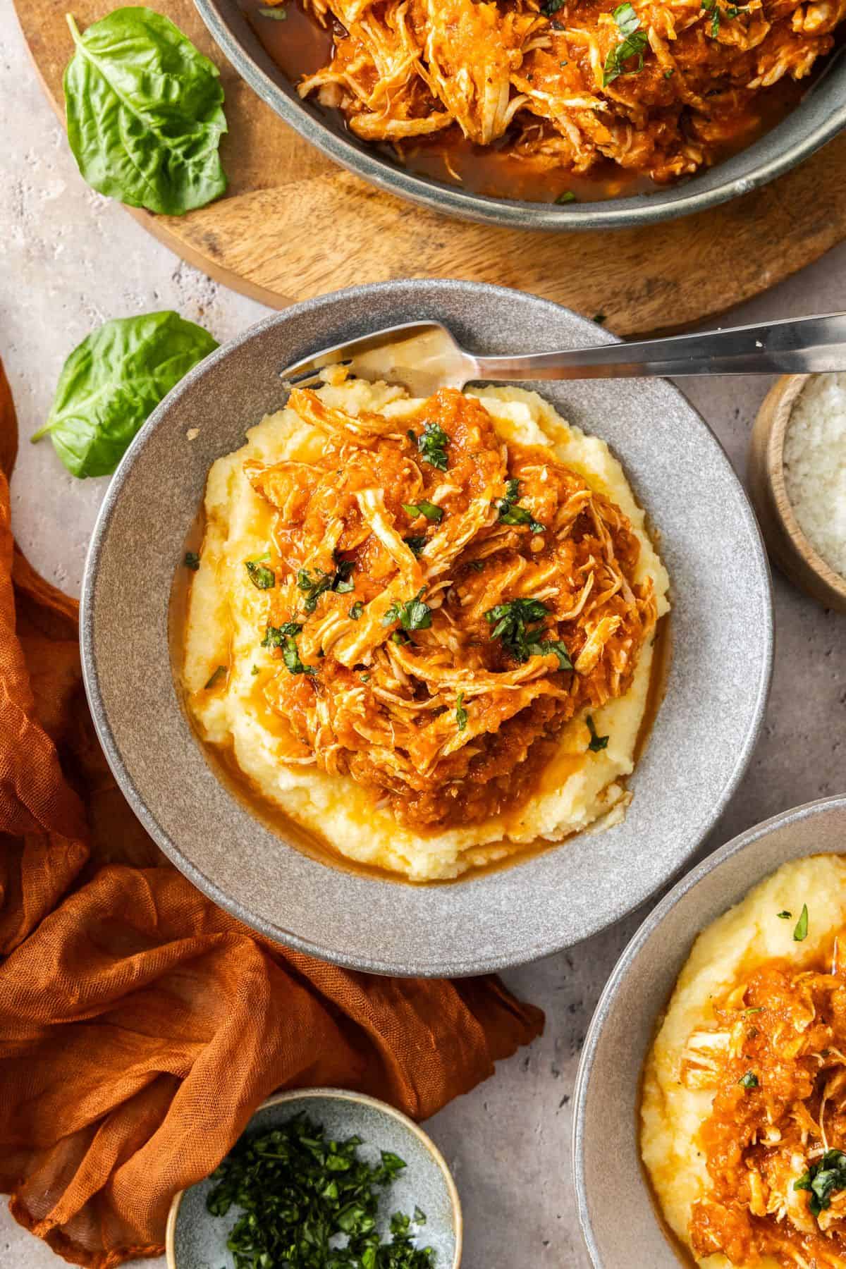 Serve of Mediterranean Pulled Chicken in a grey bowl, on a bed of creamy polenta.