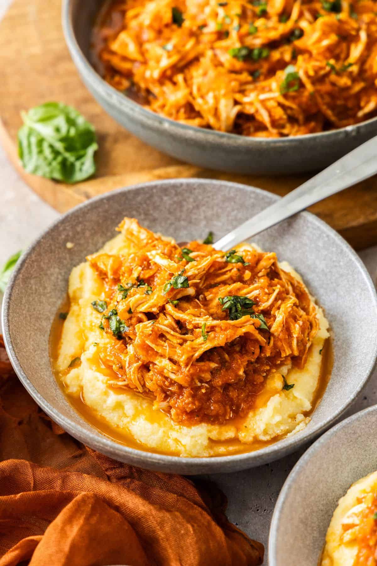 Serve of Mediterranean Pulled Chicken in a grey bowl, on a bed of creamy polenta.