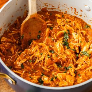 Large saucepan of Mediterranean Pulled Chicken, with a wooden spoon resting in pot.