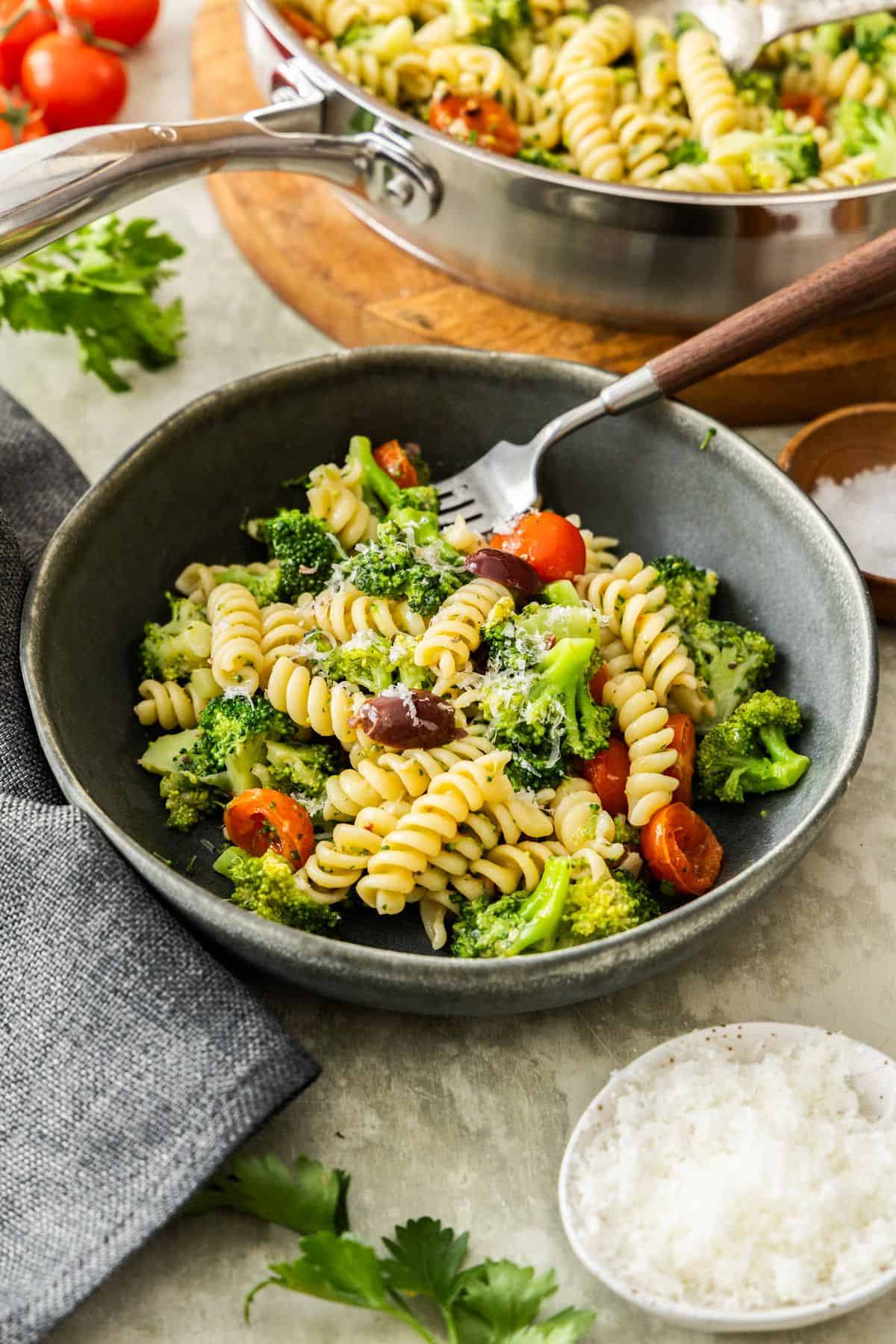 Round grey bowl of Broccoli and Tomato Pasta with a fork resting in bowl.